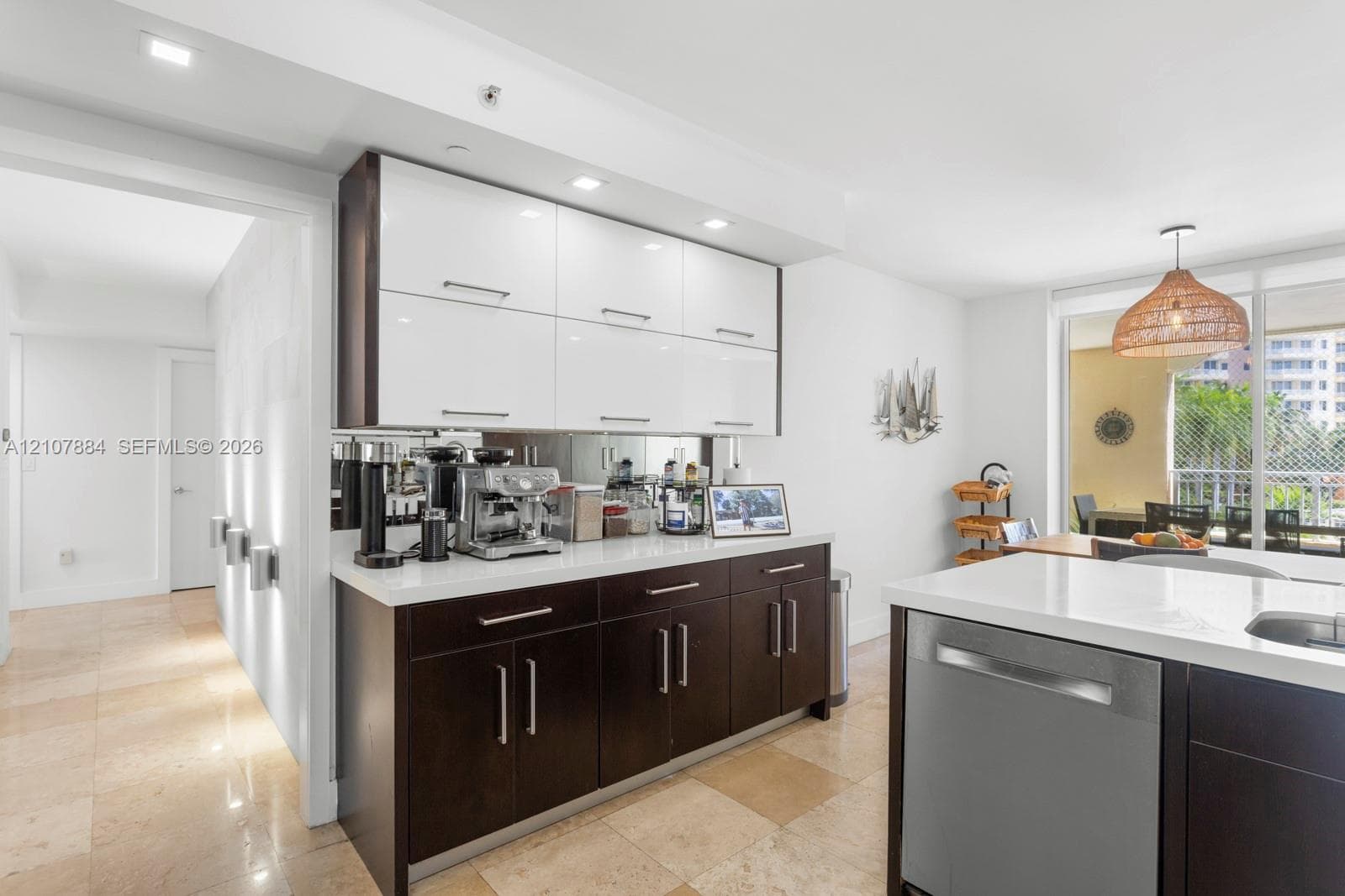 Kitchen featuring high-gloss white upper cabinetry, dark wood-finish lower cabinetry, stone countertops, a mirrored backsplash, and stone tile flooring