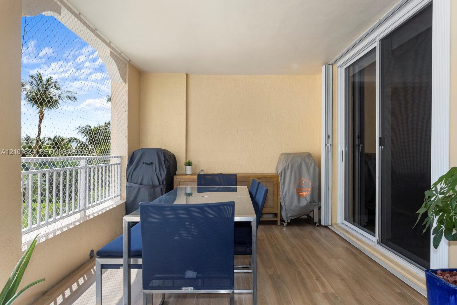 Covered balcony featuring wood-finish flooring, white metal railing, integrated screen enclosure, and sliding glass door entry