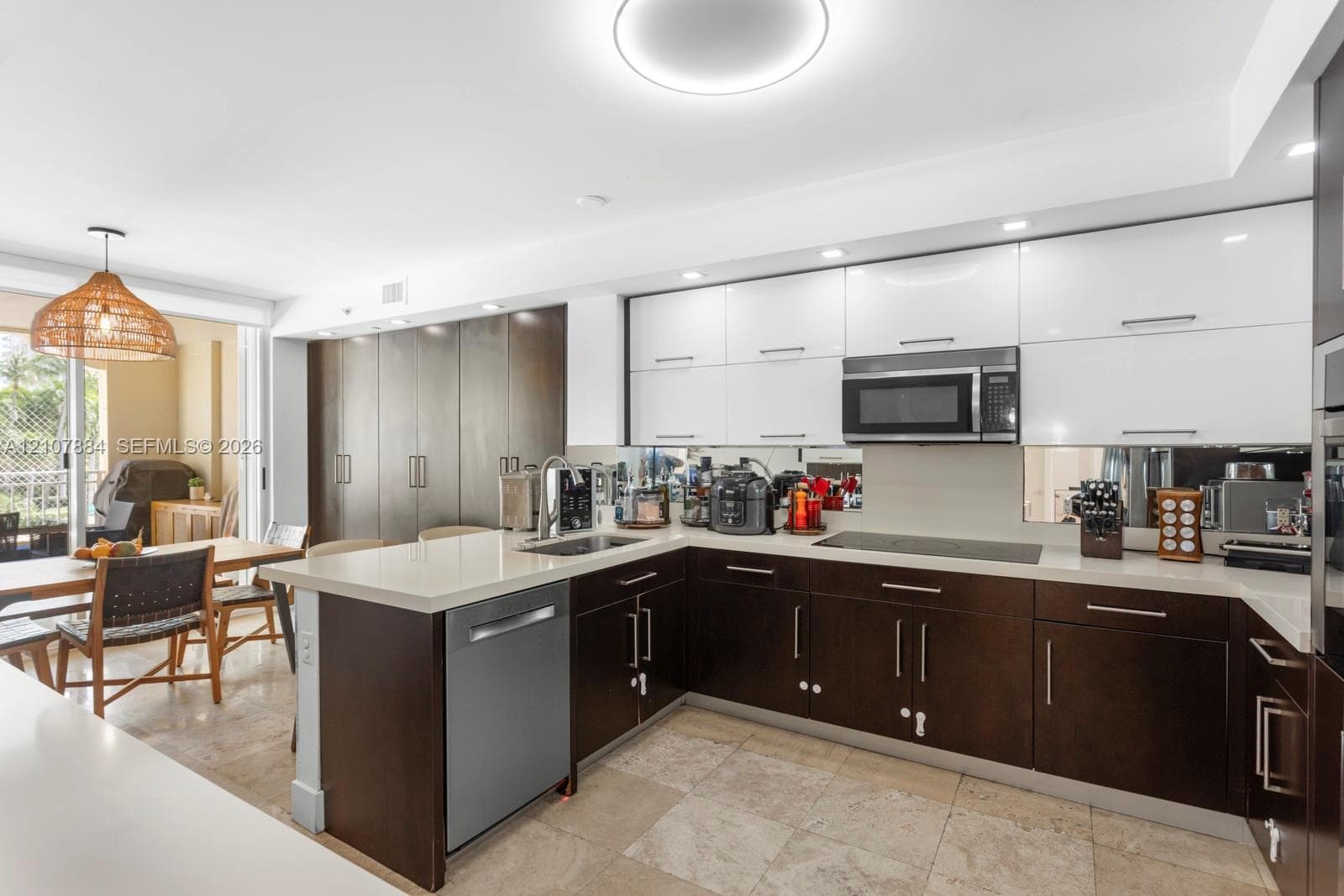 Kitchen featuring dual-tone cabinetry, stone countertops, stainless steel appliances, mirrored backsplash, and stone tile flooring