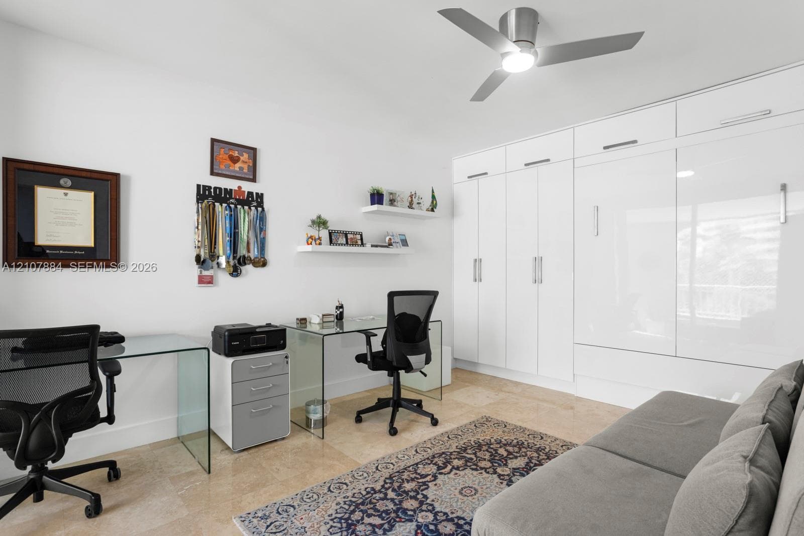 Room featuring large-format stone tile flooring, high-gloss white built-in floor-to-ceiling cabinetry, two mounted floating display shelves, and a contemporary ceiling fan with integrated lighting