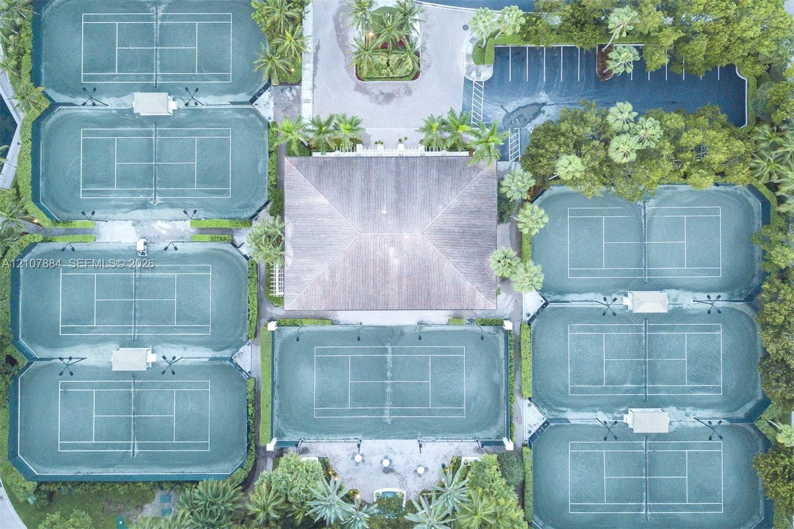 Aerial perspective featuring seven tennis courts, a central clubhouse with a hip roof, and paved surface parking