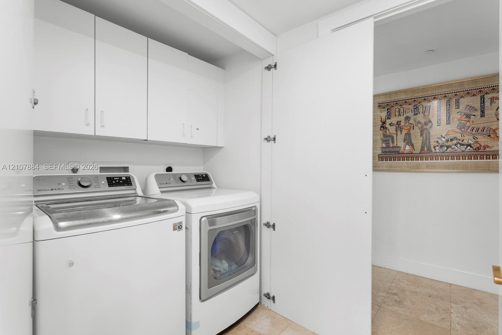 Laundry area featuring white cabinetry, stone-finish tile flooring, and a neutral palette