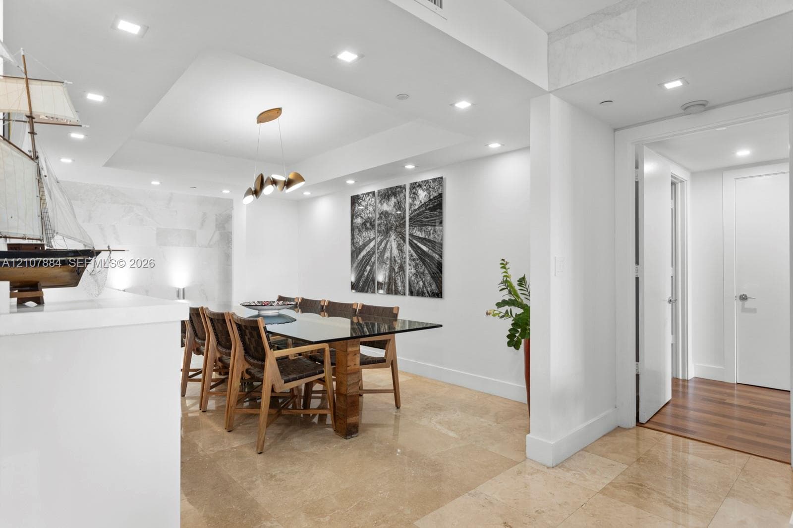 Recessed ceiling lighting, tray ceiling detail, stone tile flooring, and metallic chandelier fixture