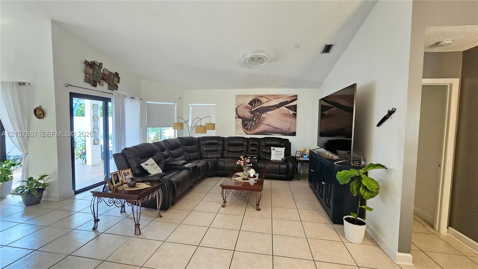Living area featuring vaulted ceilings, neutral ceramic tile flooring, and sliding glass doors providing outdoor access