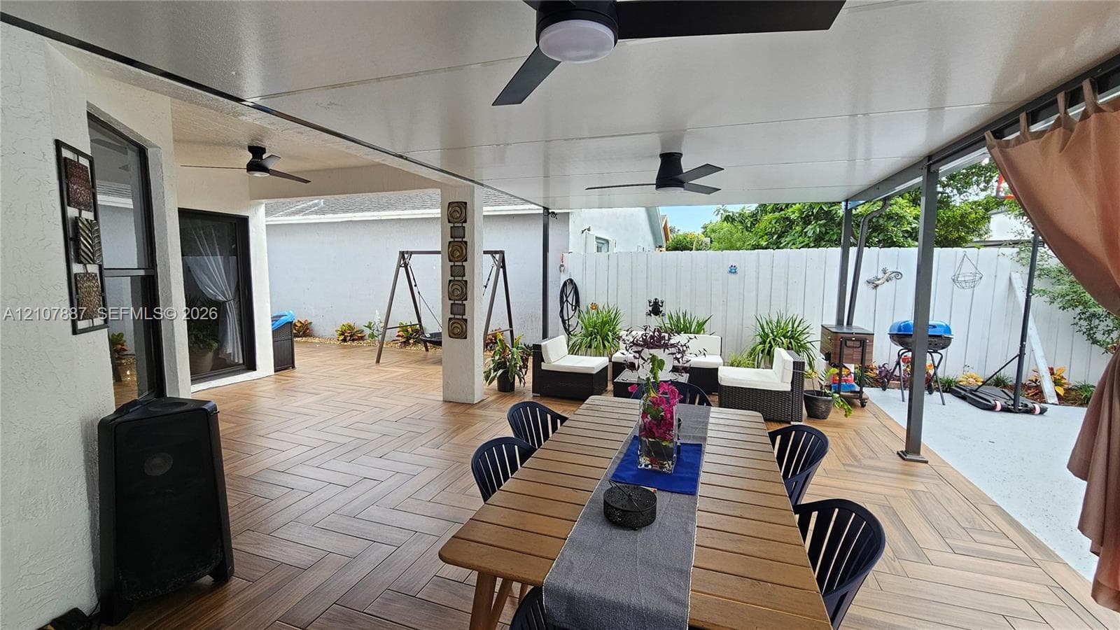 Covered patio featuring herringbone-patterned tile flooring, multiple ceiling-mounted fans, and white privacy fencing