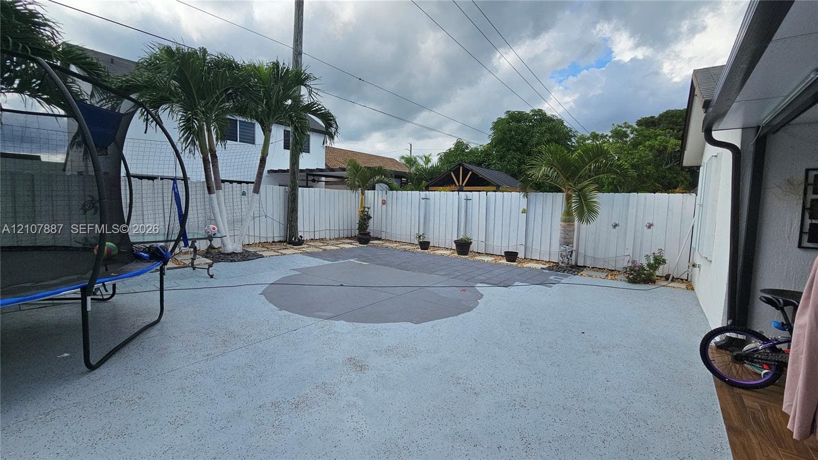 Backyard featuring a paved patio, perimeter vinyl fencing, and palm trees