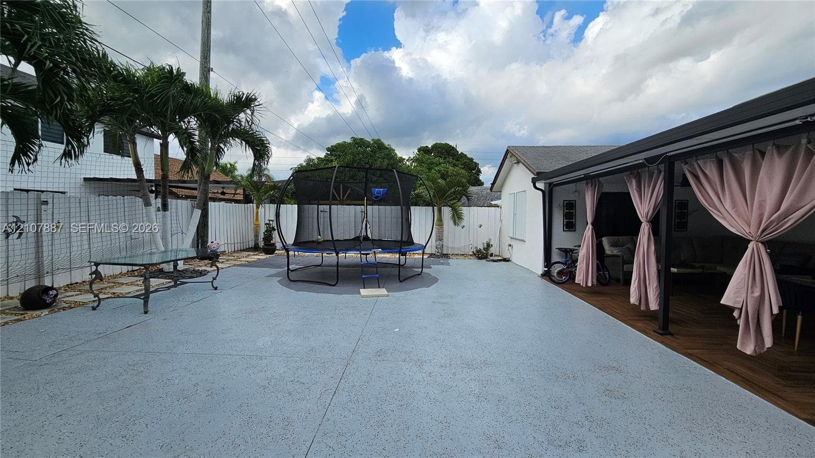 Expansive outdoor patio with concrete surfacing, covered rear porch featuring wood-finish flooring, and white vinyl perimeter fencing