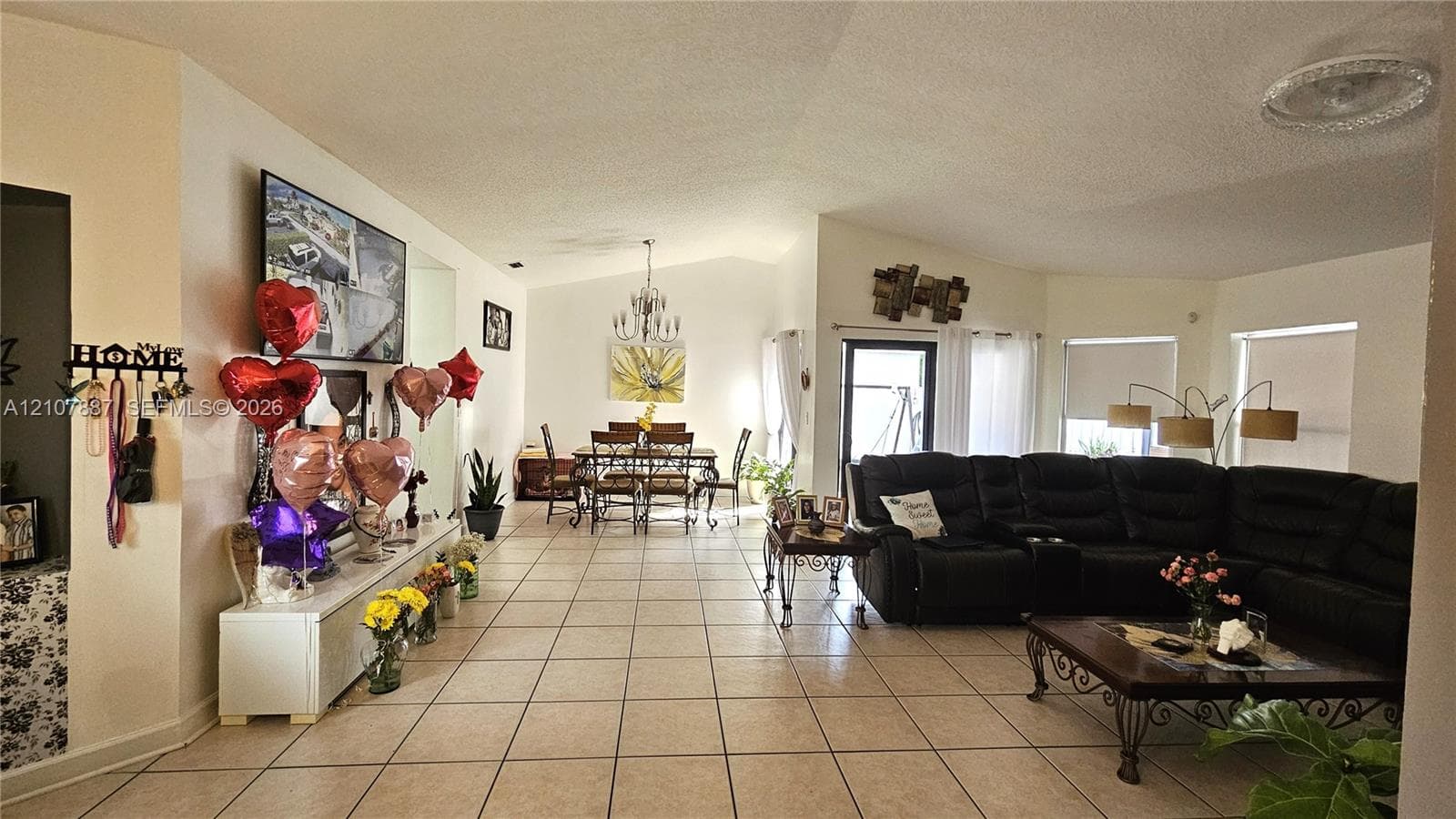 Open-concept floor plan featuring vaulted ceilings, neutral ceramic tile flooring, and a decorative tiered chandelier