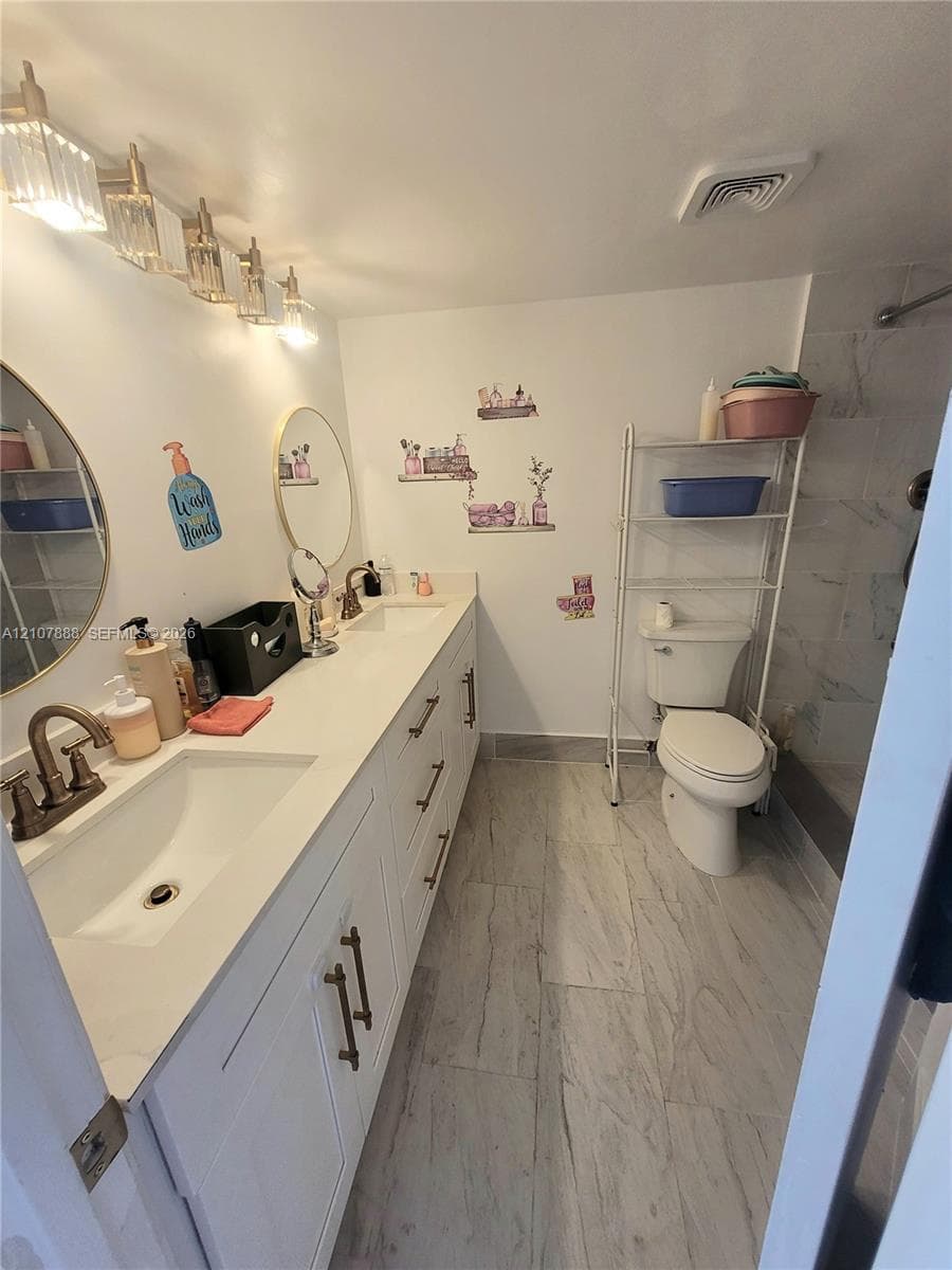 Dual-sink vanity with white cabinetry, light-toned stone-finish countertop, round wall-mounted mirrors, and multi-light fixture