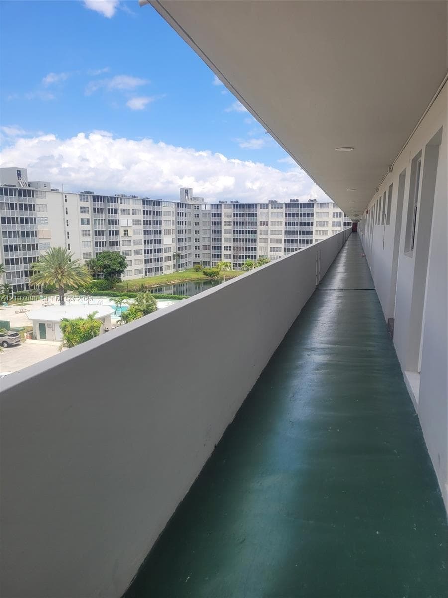 Covered exterior walkway featuring a painted concrete floor, solid masonry railing, and overhead lighting