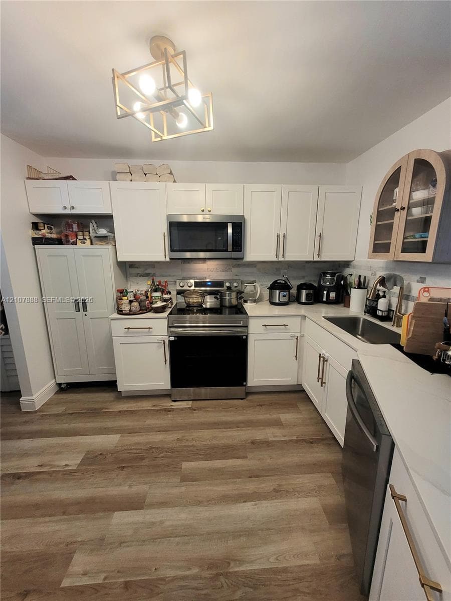 Kitchen featuring white Shaker-style cabinetry, stainless steel appliances, wood-finish flooring, stone-style countertops, and a geometric-frame ceiling light fixture