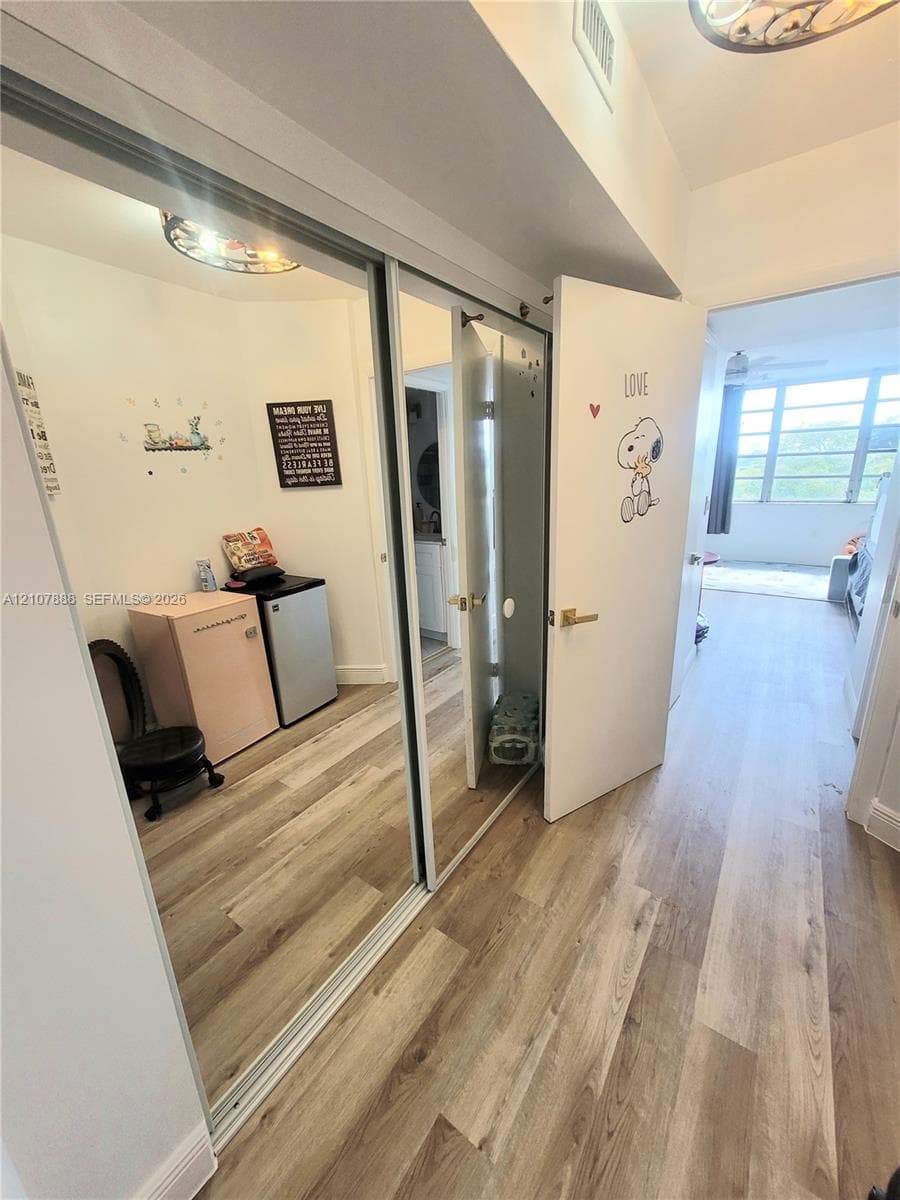 Wood-finish flooring throughout, floor-to-ceiling mirrored sliding closet doors, flush-mount circular lighting, and a white interior door with metallic hardware