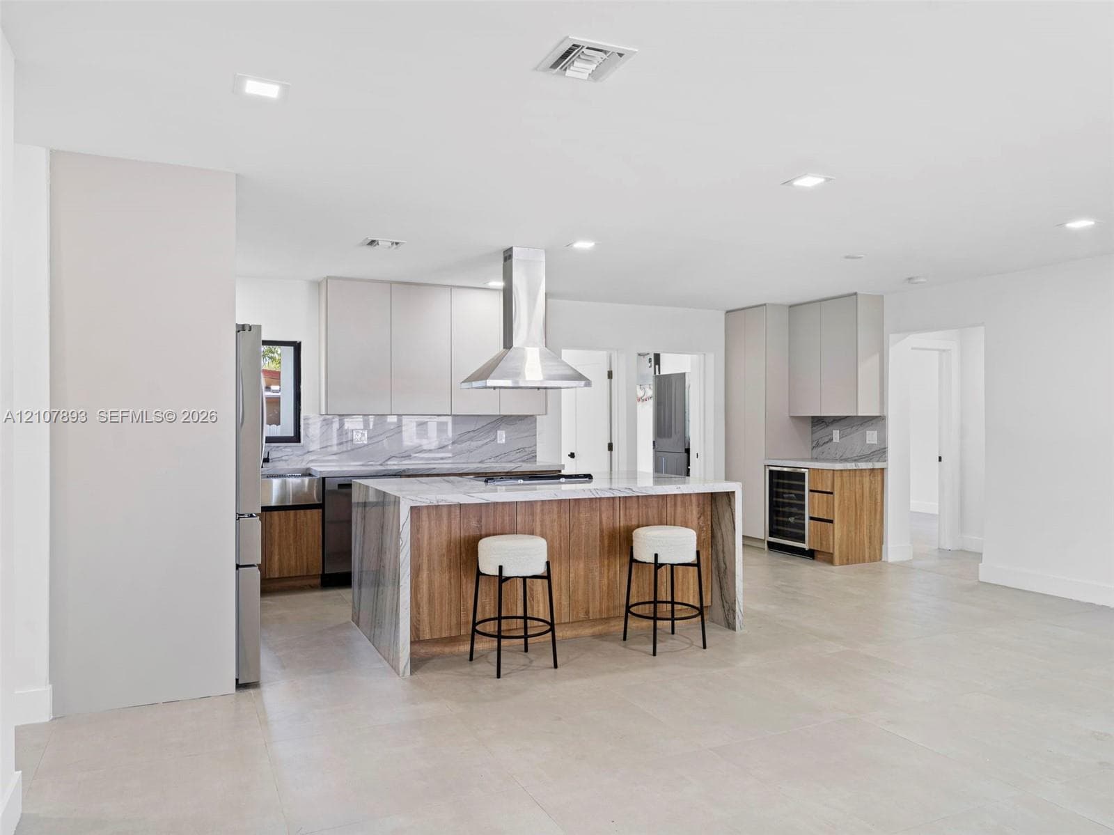 Kitchen featuring flat-panel cabinetry, a waterfall-edge stone island, stainless steel range hood, built-in wine refrigerator, and tile flooring