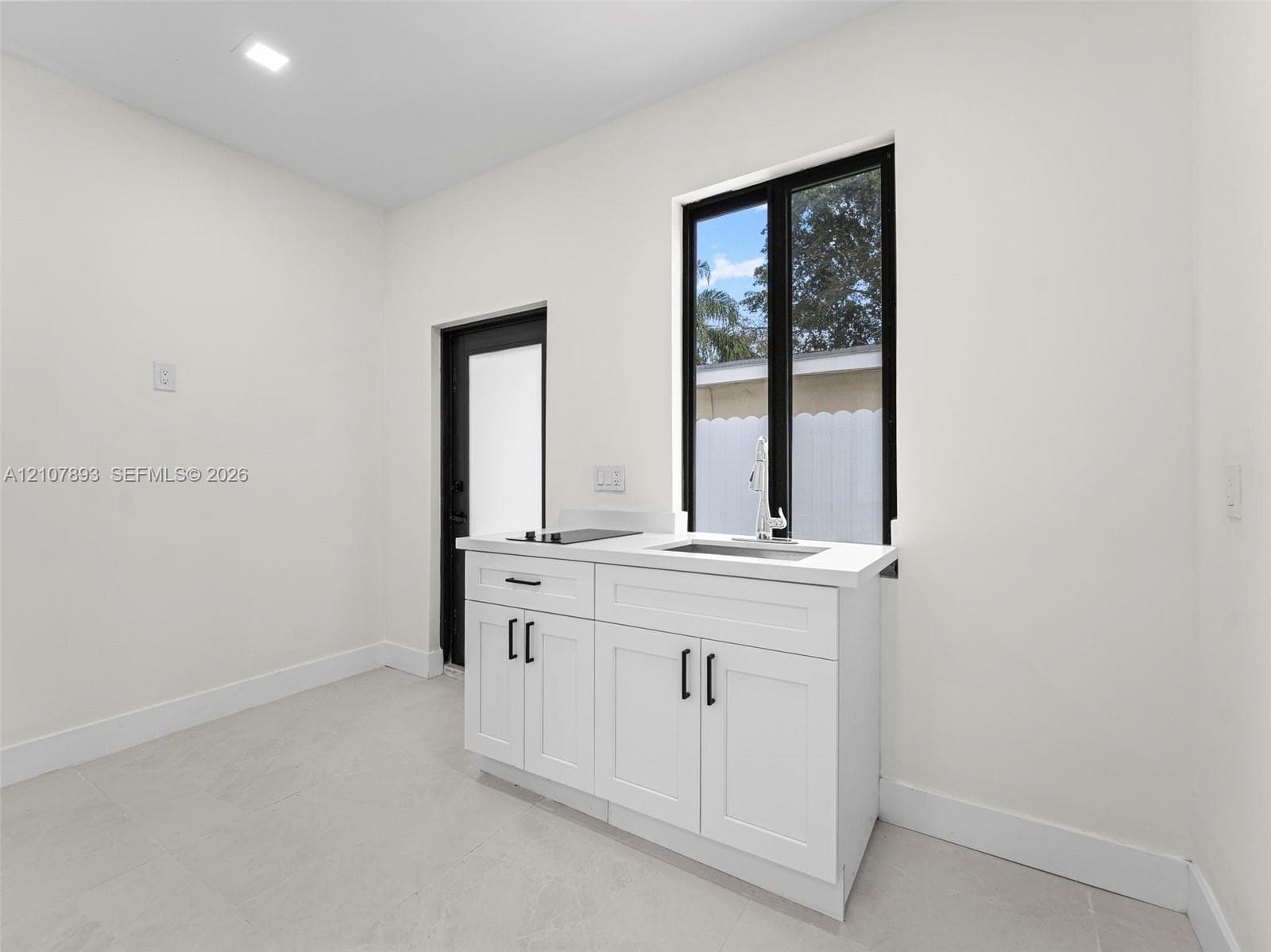 Shaker-style white cabinetry with matte black hardware, stone-finish countertop, integrated stainless steel sink, and recessed ceiling lighting