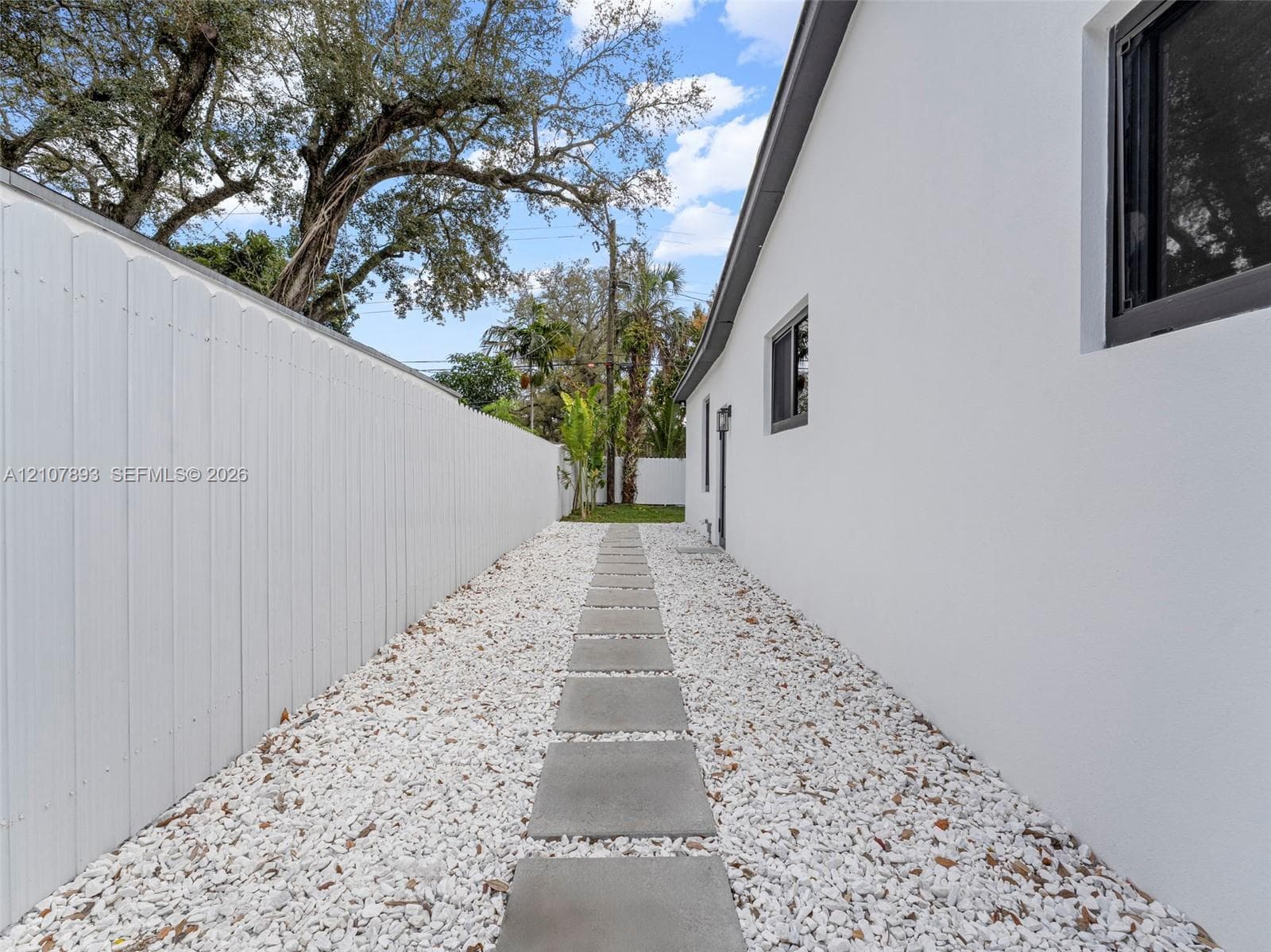 Side yard featuring a concrete paver walkway, white rock ground cover, and a solid white privacy fence