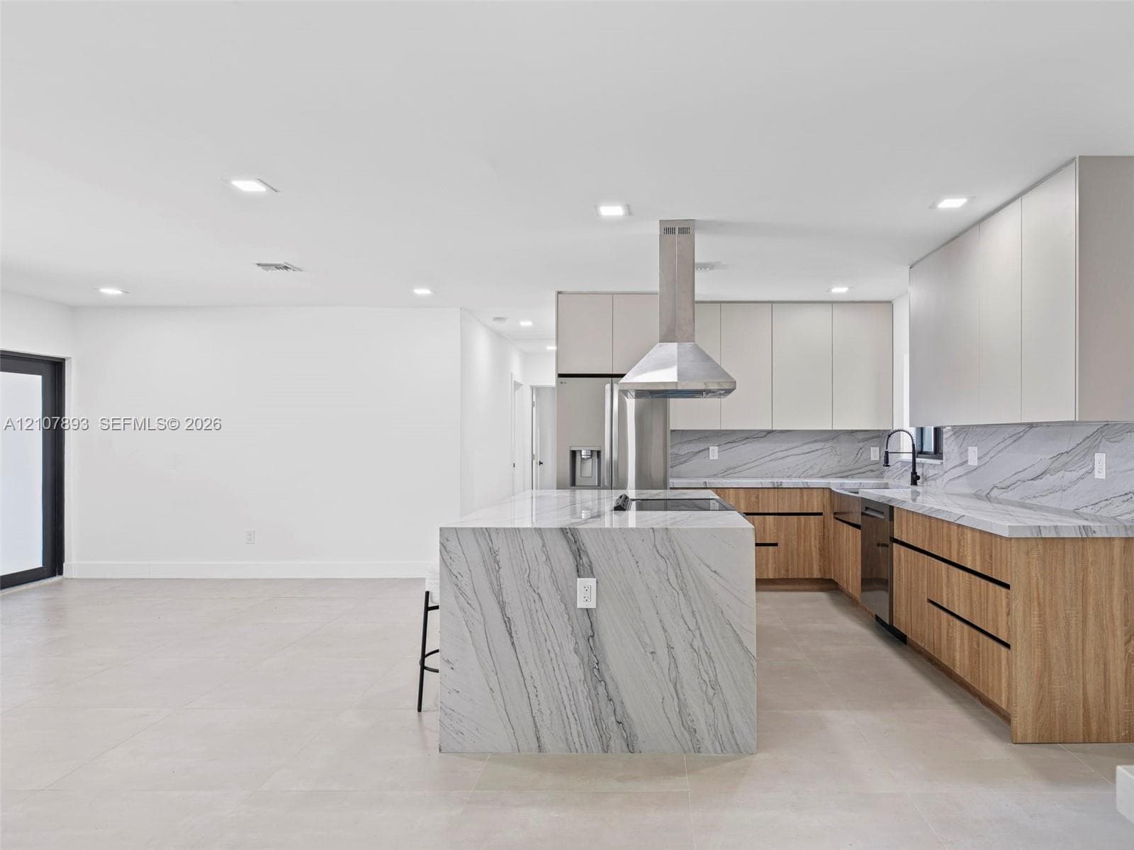 Modern kitchen featuring flat-panel cabinetry, stone-patterned countertops with matching waterfall island, stainless steel range hood, and large-format tile flooring