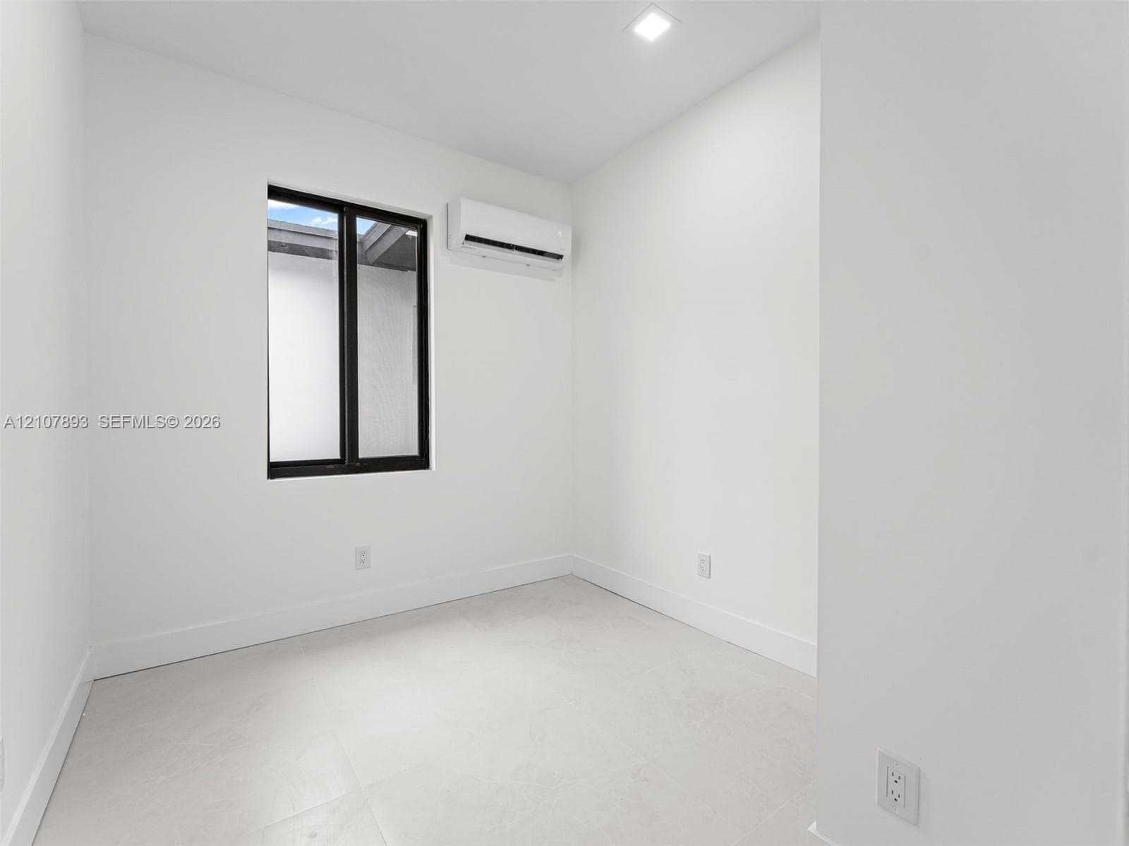 Neutral room featuring light-toned tile flooring, recessed ceiling lighting, a wall-mounted ductless air conditioning unit, and a window with a dark frame