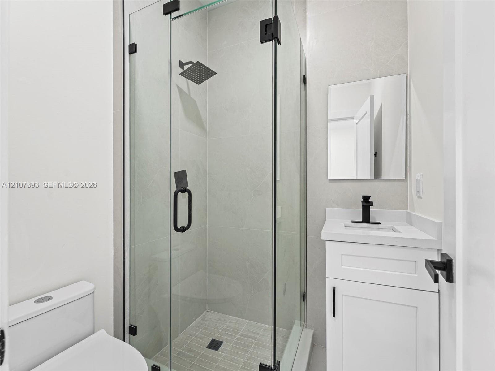 Walk-in shower with a glass enclosure, square rain-style shower head, white vanity cabinet with stone-finish countertop, square undermount sink, and matte black hardware