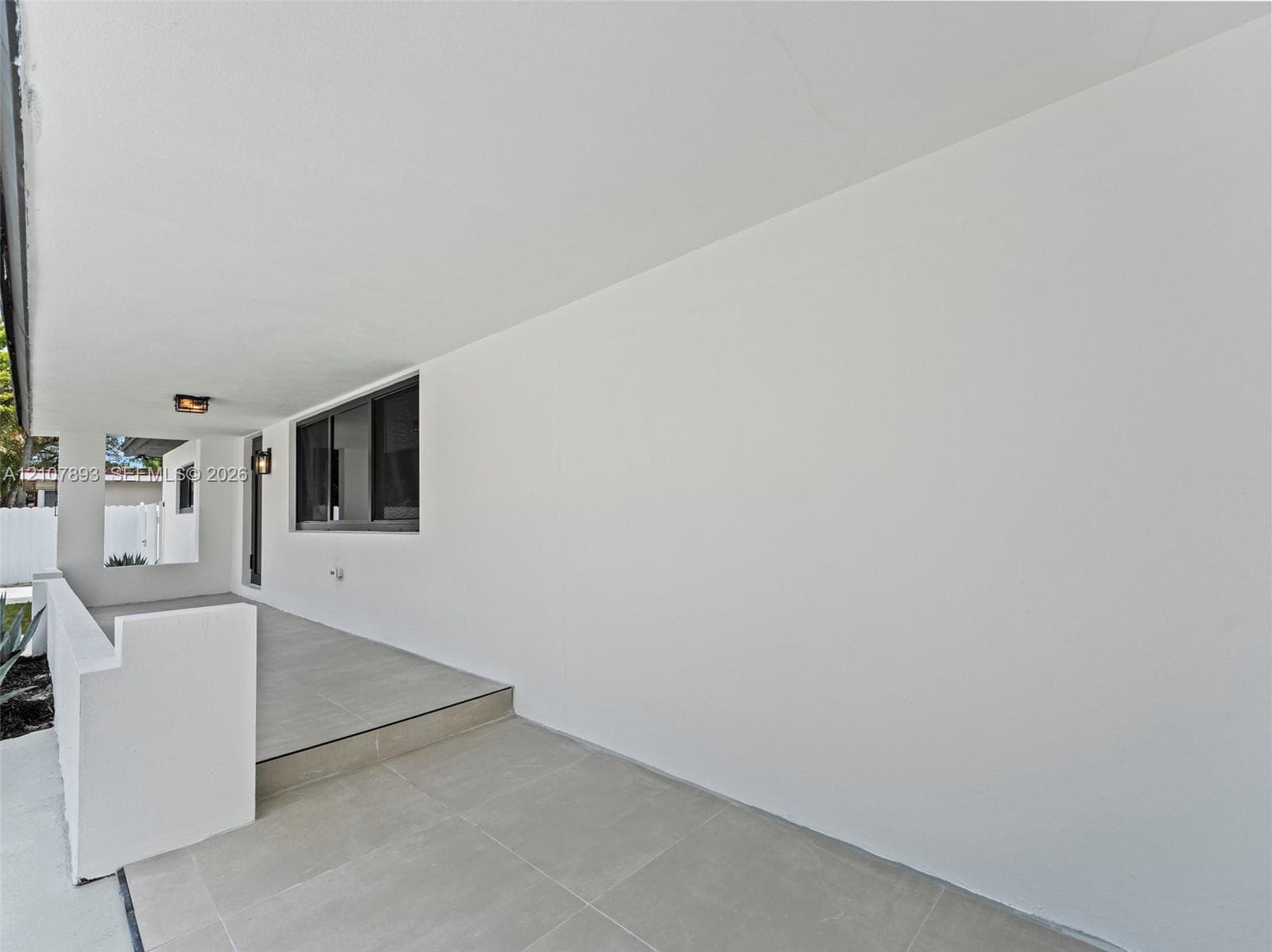 Covered porch featuring large-format tile flooring, a solid masonry partition wall, and wall-mounted exterior lighting fixtures