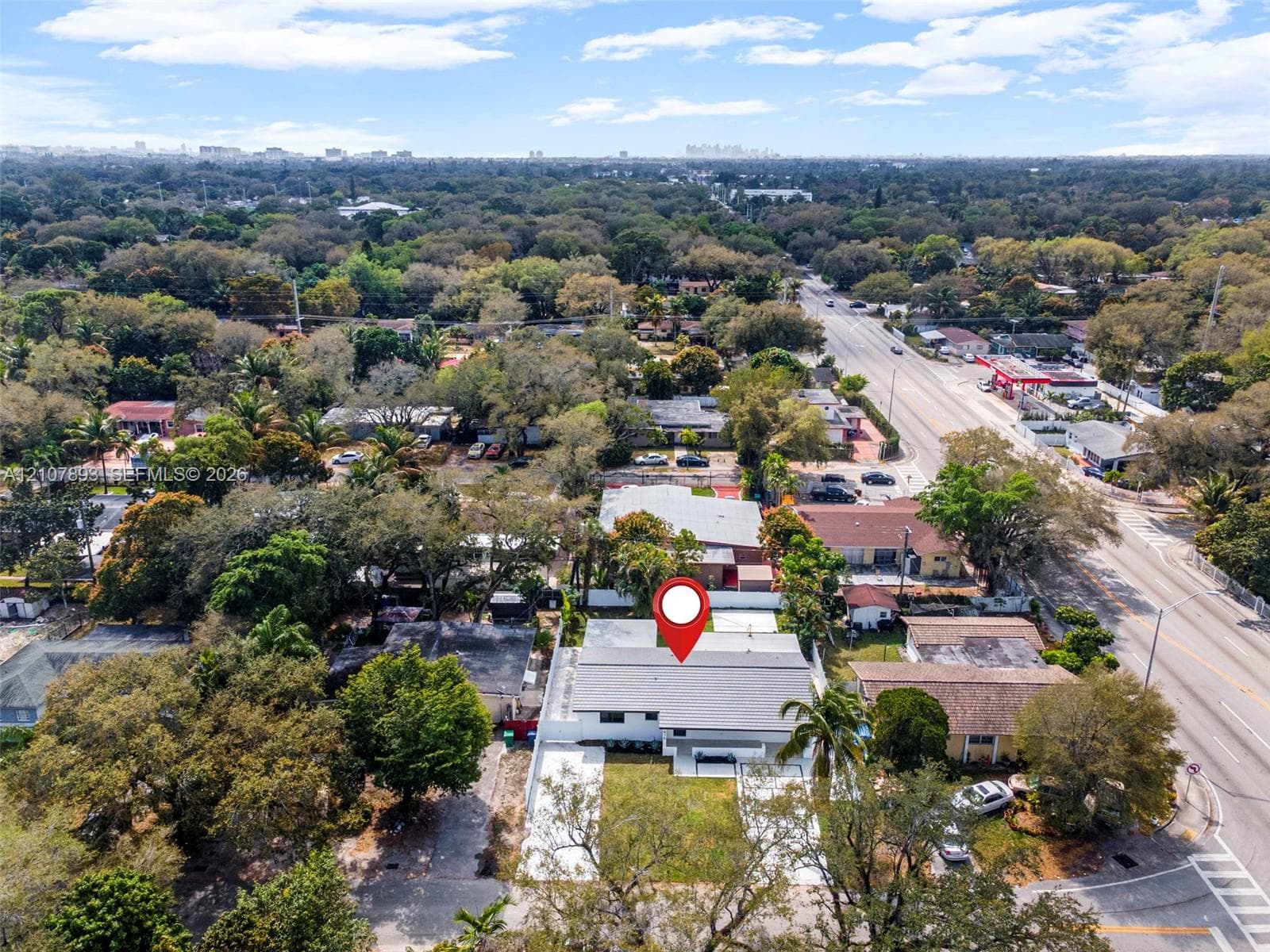 Aerial perspective featuring a single-story residence with a light-toned exterior, gabled roof, paved driveway, and perimeter fencing