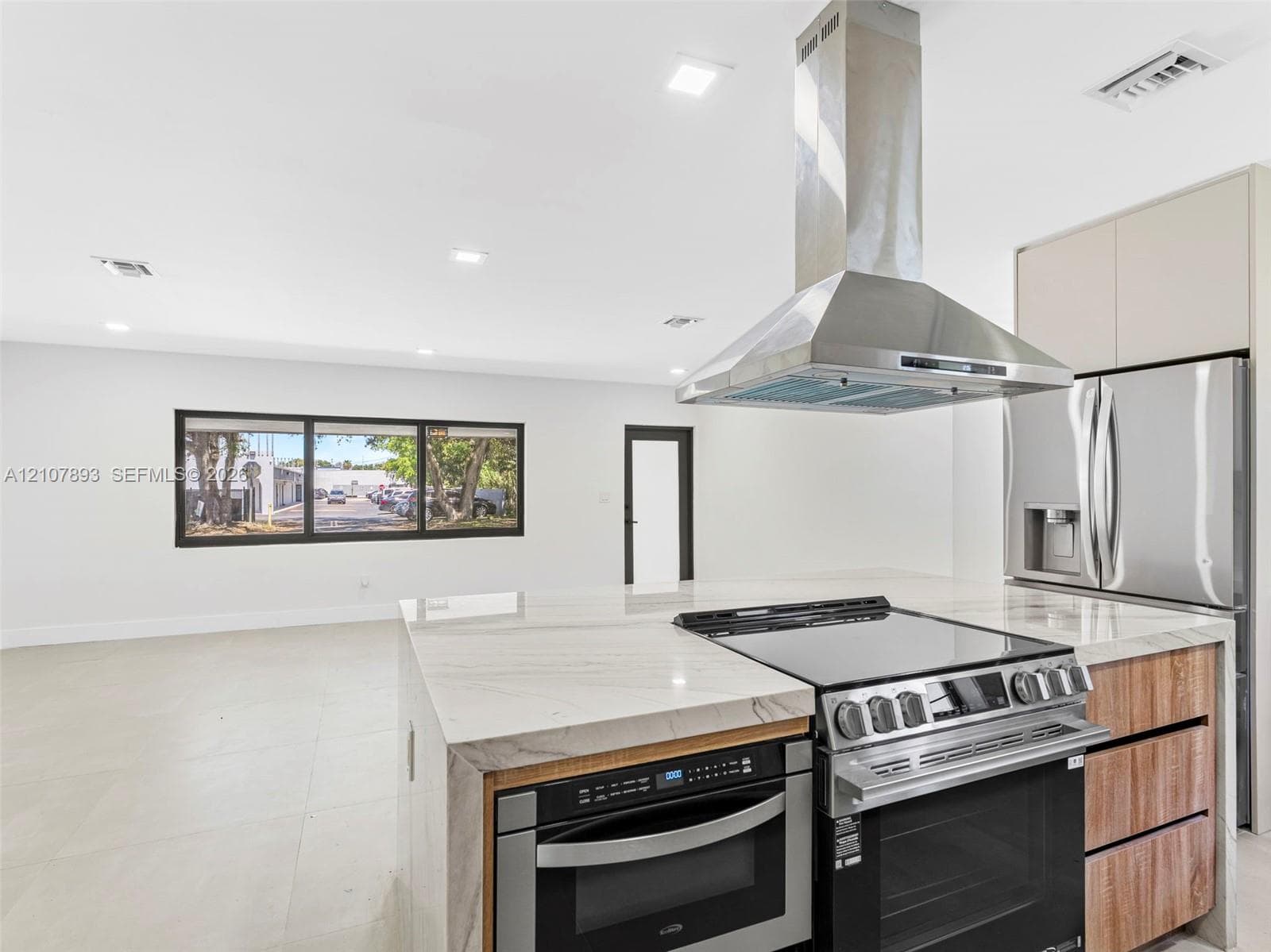 Kitchen featuring an island with a waterfall-edge countertop, stainless steel range hood, integrated built-in oven, and wood-finish cabinetry