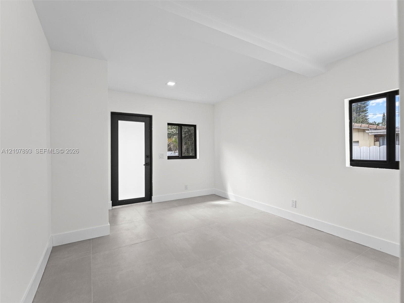 Neutral interior space featuring large-format tile flooring, matte black window and door frames, and flush-mount recessed lighting