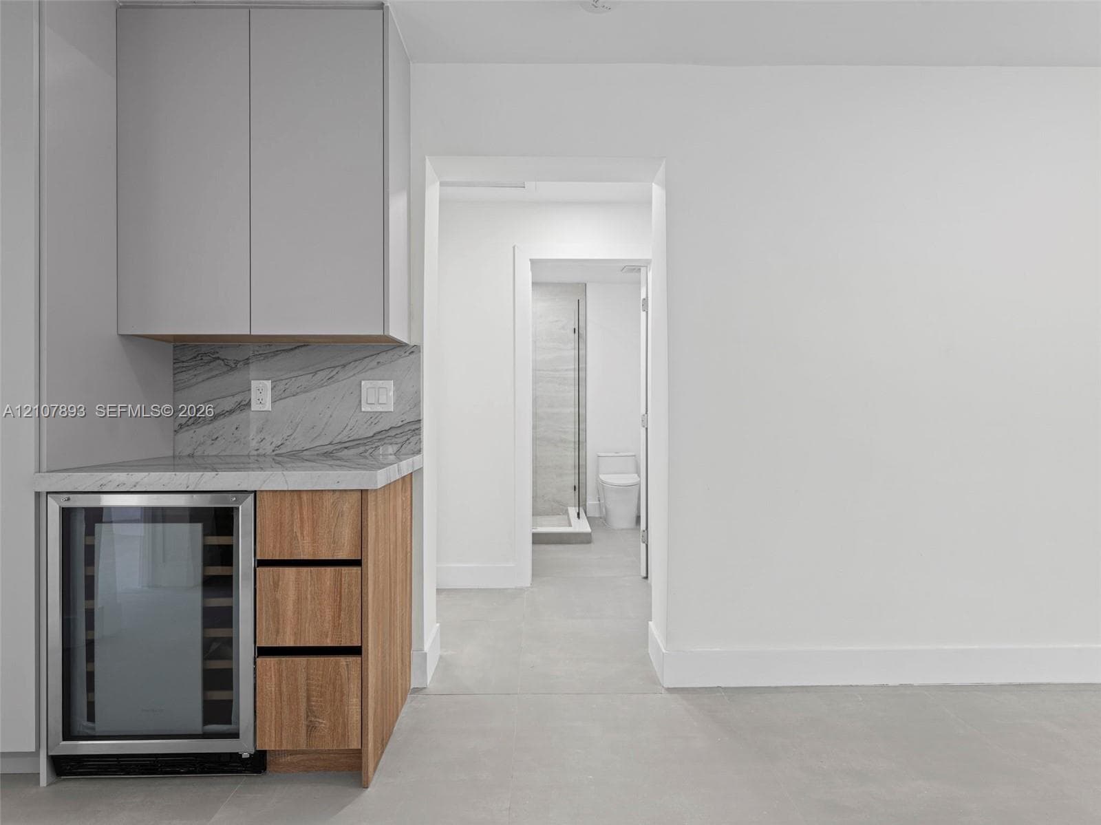 Built-in cabinetry featuring light-toned wood base and matte-finish upper cupboards, stone-surfaced countertop, integrated beverage refrigerator, and stone-tiled flooring throughout
