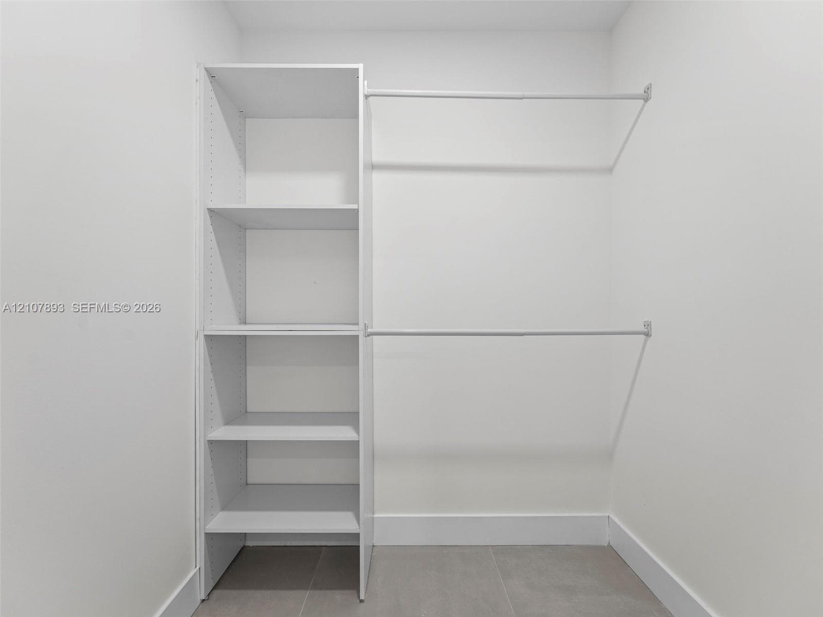 Walk-in closet featuring white built-in shelving and dual horizontal hanging rods over tile flooring