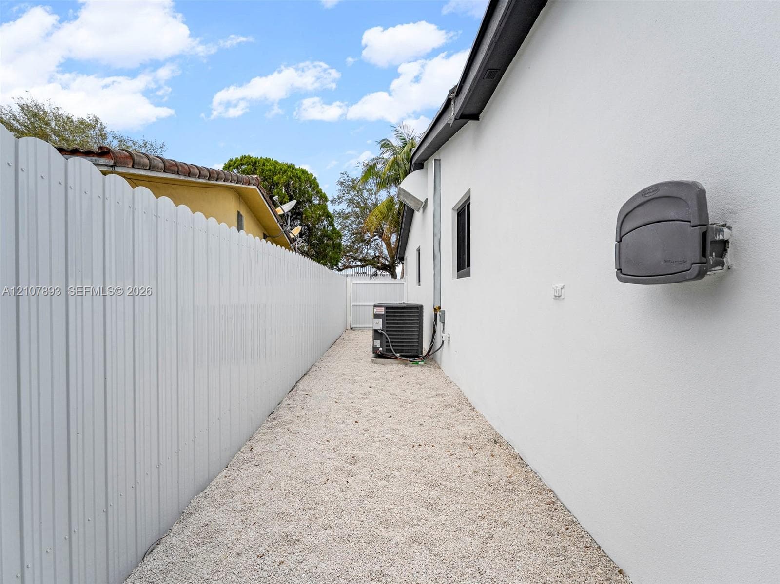 Exterior side yard featuring white stucco siding, full-height white vinyl fencing, gravel ground cover, and a dedicated HVAC unit