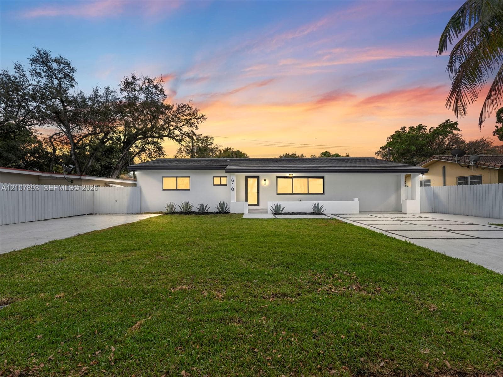 Single-story residence featuring a smooth stucco exterior, low-pitch roofline, paver driveway with decorative grass inlays, manicured lawn, and perimeter privacy fencing
