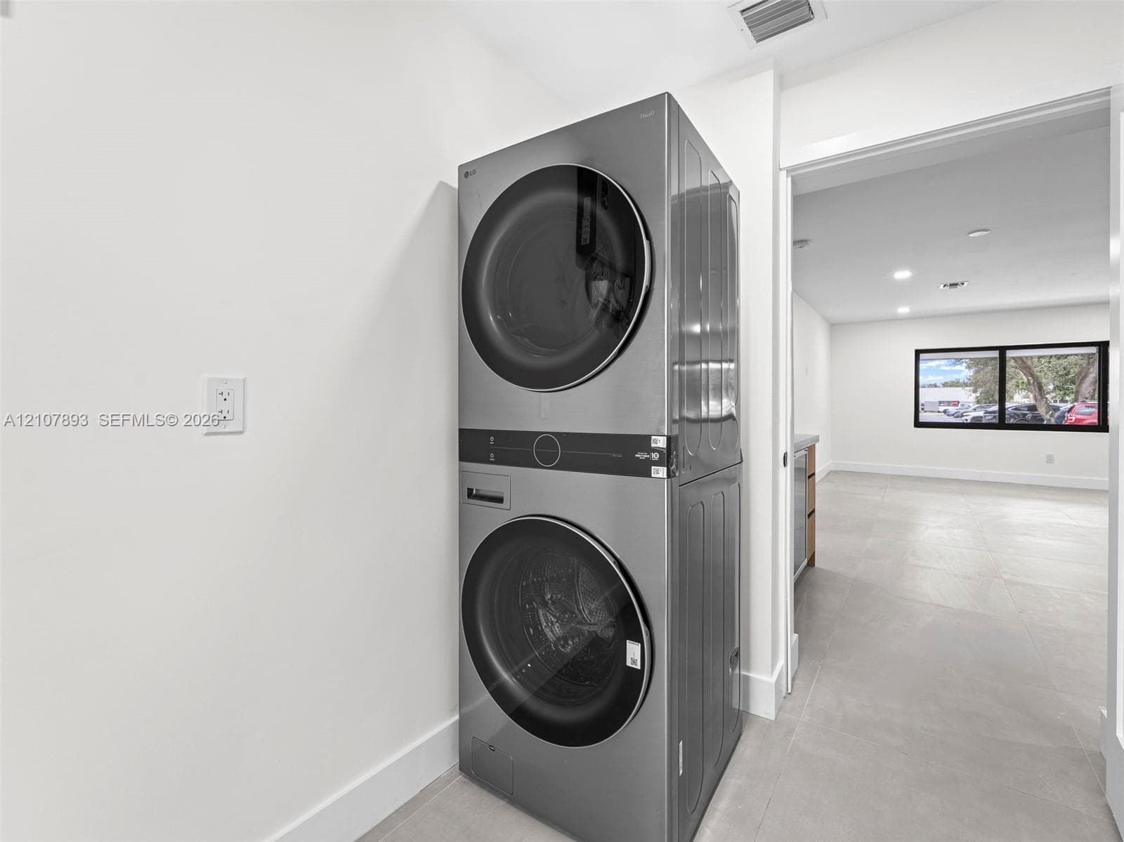 Stainless steel stacked laundry unit featuring front-loading washer and dryer with integrated digital controls and large-format tile flooring