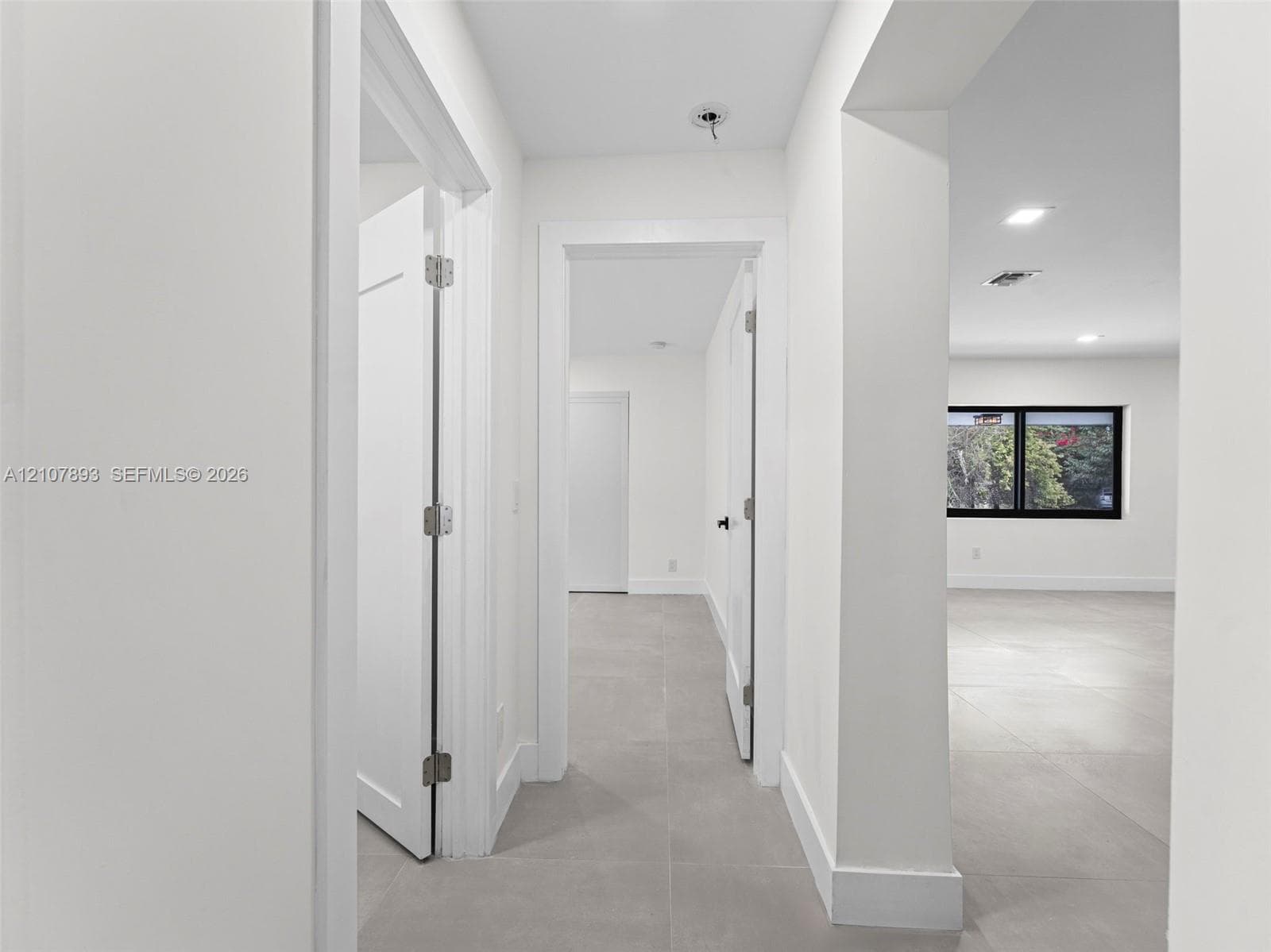 Neutral-toned large-format tile flooring, crisp white walls, recessed ceiling lighting, and black-trimmed window frames