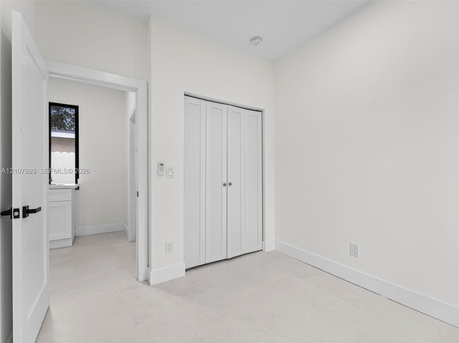 Neutral-toned interior featuring crisp white walls, tile flooring, and white bifold closet doors with metallic hardware