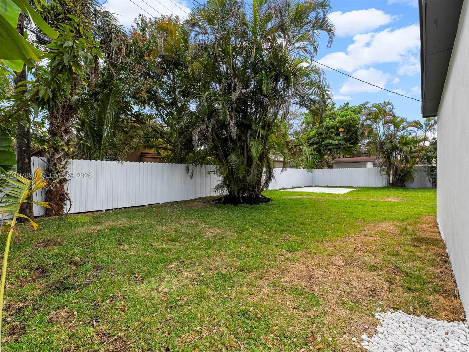 Backyard featuring a grass lawn, white vinyl fencing, mature landscaping, and a concrete patio slab