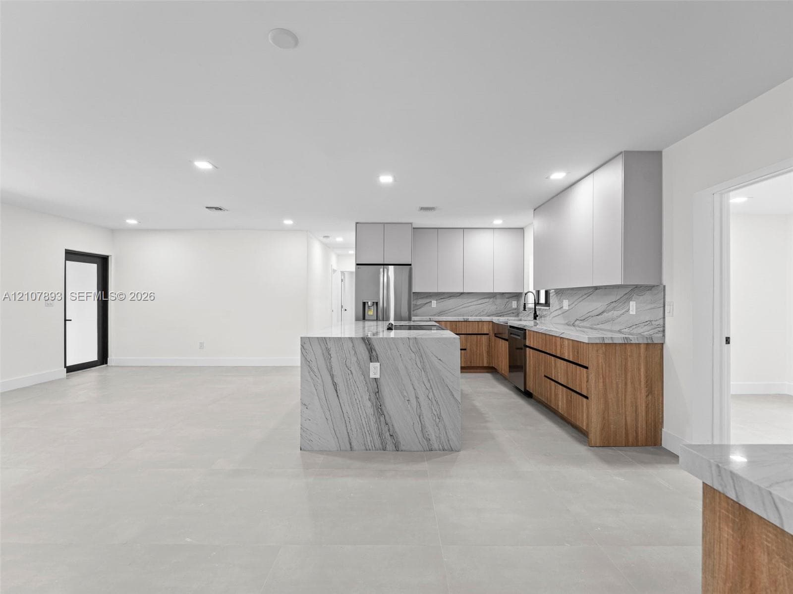 Modern kitchen featuring a central island with a stone waterfall countertop, wood-finish cabinetry, matte light gray upper cabinets, and a matching stone backsplash