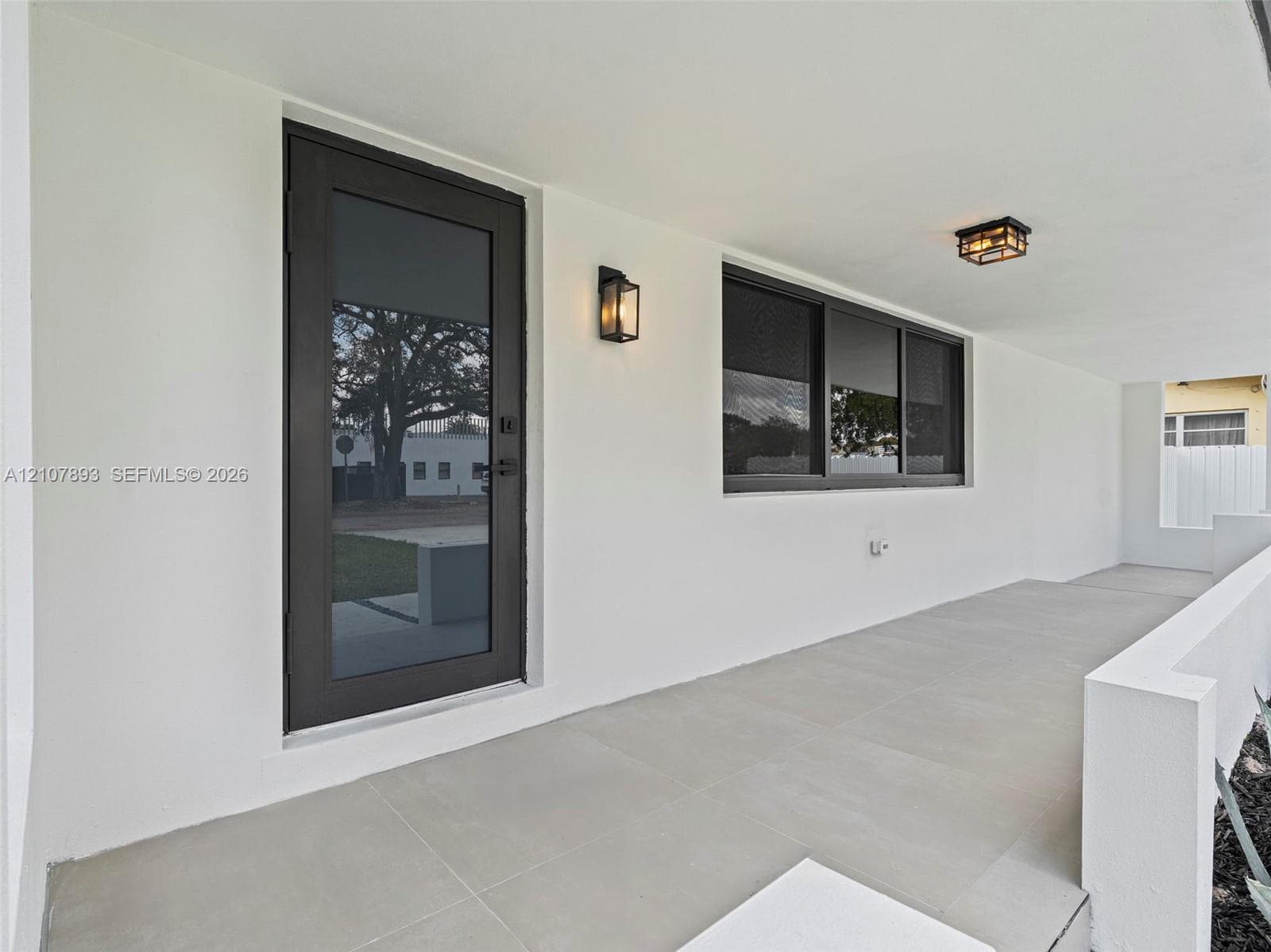 Covered entryway featuring large-format tile flooring, a full-glass entry door with dark trim, dual wall-mounted lanterns, and a flush-mount ceiling fixture