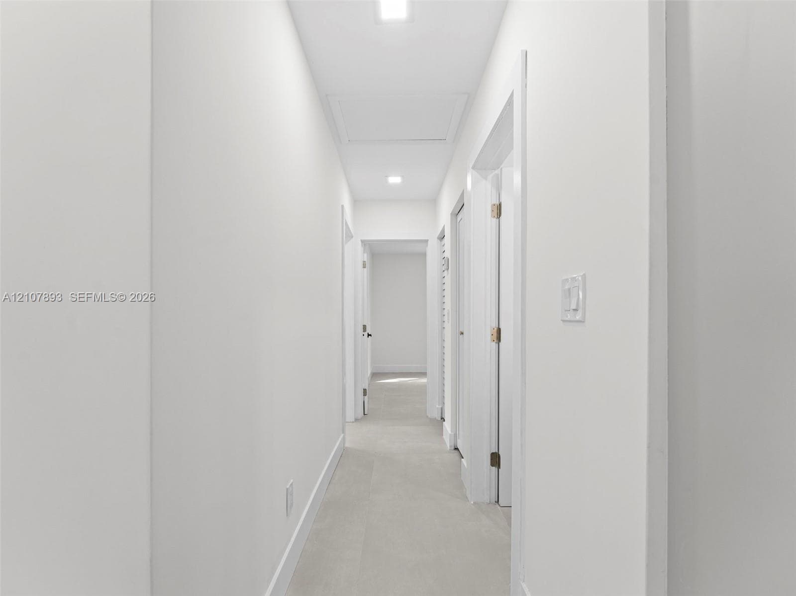 Hallway featuring neutral-toned tile flooring, recessed ceiling lighting, and crisp white wall finishes