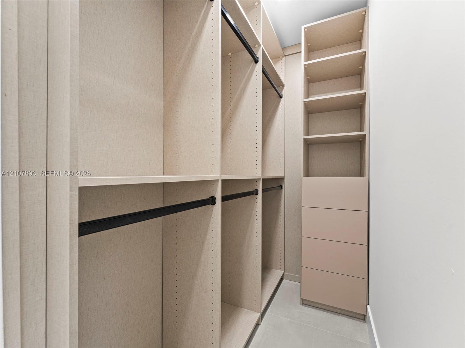 Custom reach-in closet featuring floor-to-ceiling shelving, integrated drawer stack, multiple hanging rods with matte black finish, and textured light-toned cabinetry