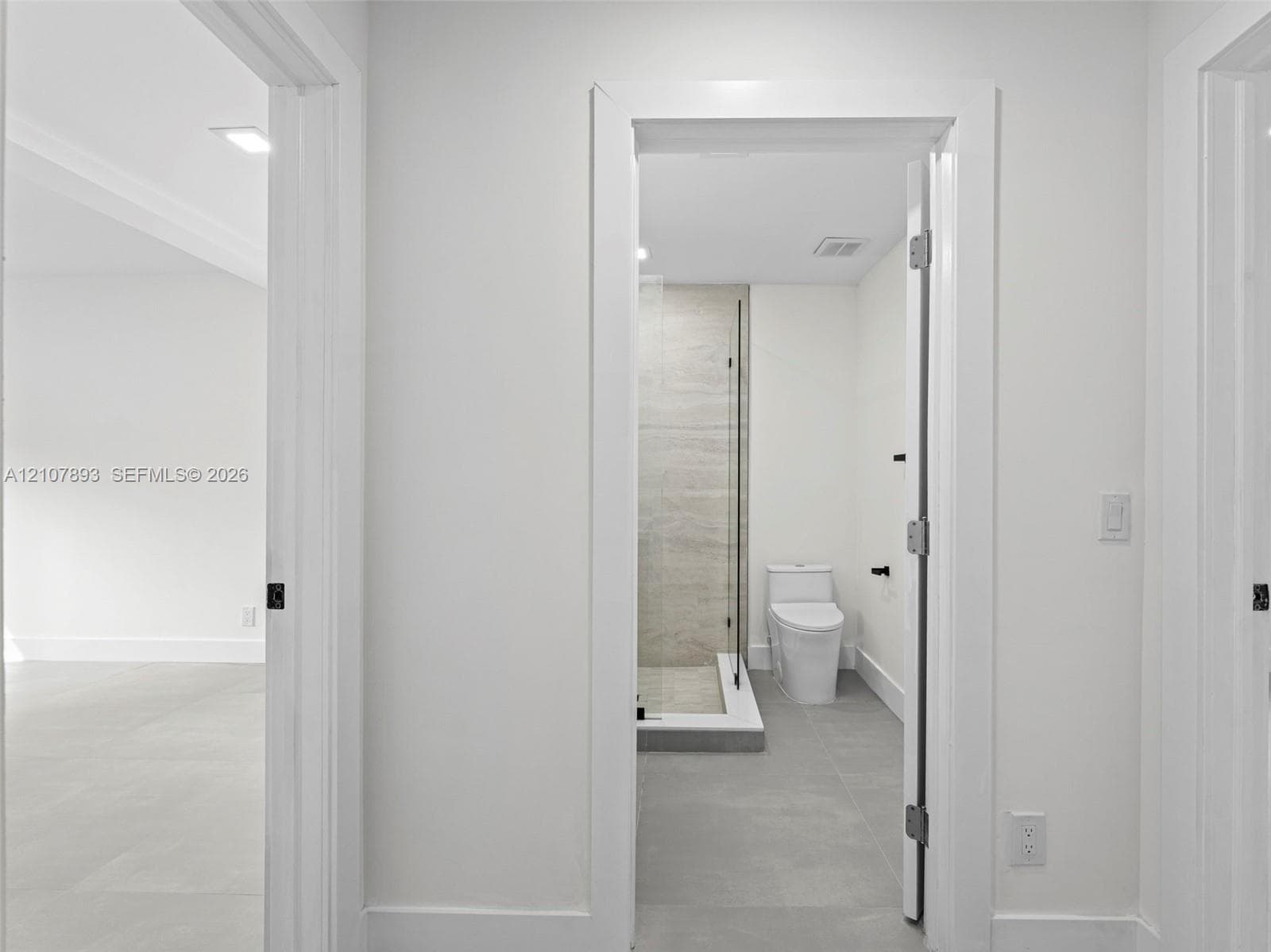 Bathroom featuring a glass-enclosed shower with large-format wall tile, a two-piece toilet, and grey tile flooring