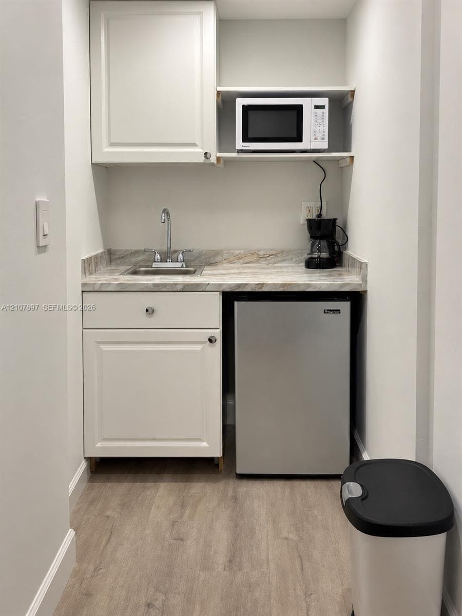Wet bar featuring white cabinetry, stone-patterned countertop, integrated under-counter refrigerator, stainless steel sink with chrome faucet, and open upper shelving