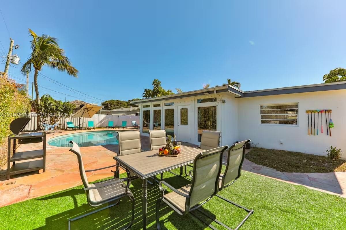 Backyard featuring a custom-shaped pool, natural stone patio, artificial turf lawn, and perimeter fencing