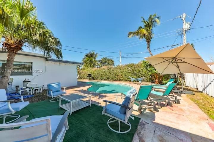Backyard oasis featuring a curvilinear inground swimming pool, stone-paver patio, perimeter privacy hedge, and mature palm trees