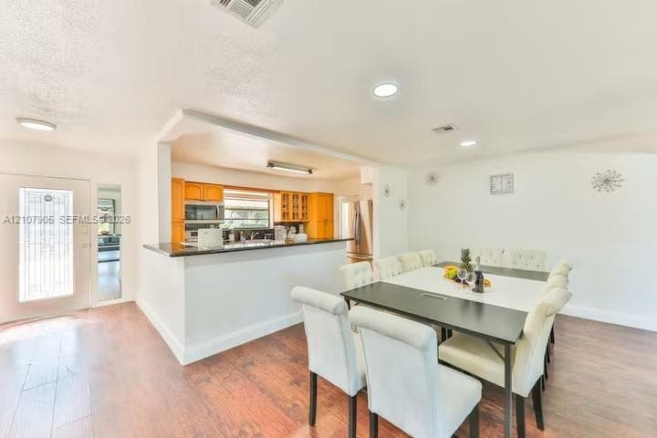 Kitchen featuring wood-finish cabinetry, dark solid-surface countertops, and recessed lighting, complemented by wood-finish flooring and a glass-paneled entry door