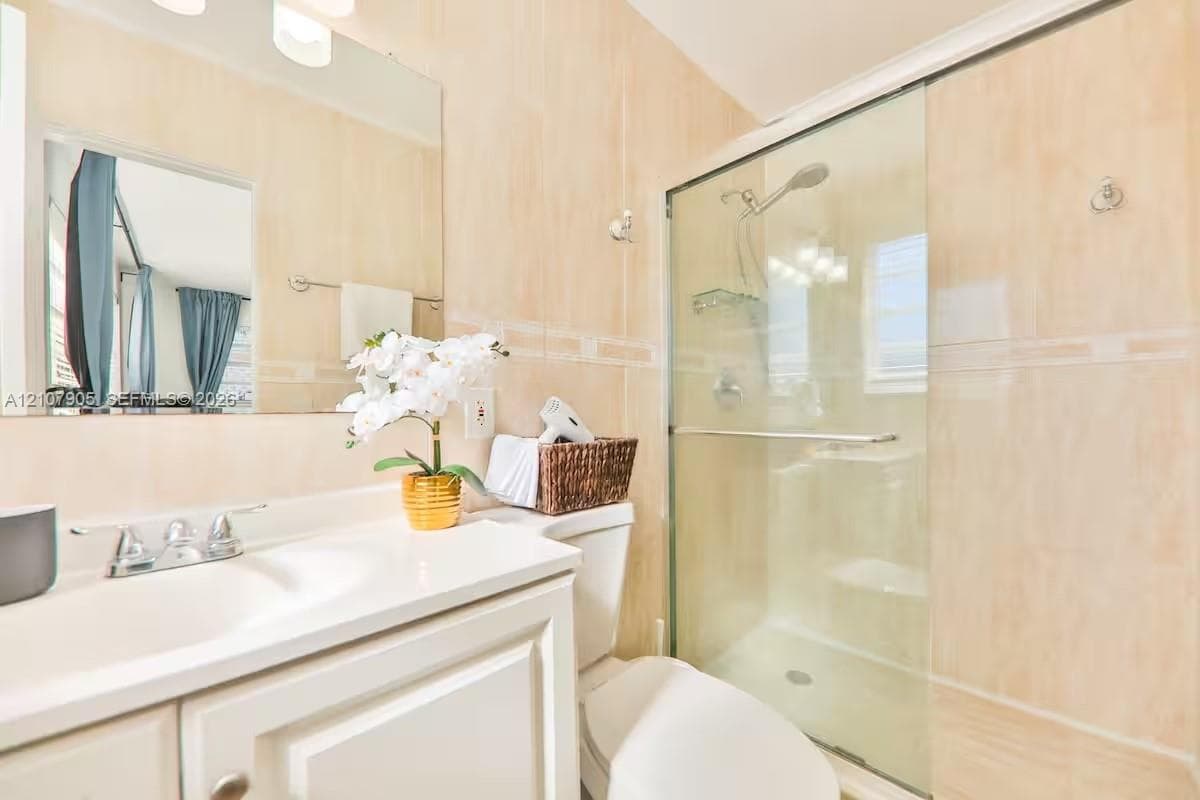 Bathroom featuring a white vanity with an integrated basin, wall-to-wall mirror, and a walk-in shower enclosed by sliding glass doors with tile surround