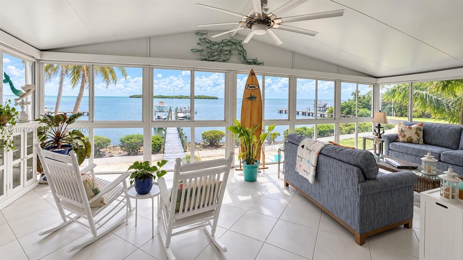 Screened lanai featuring large-format ceramic tile flooring, a vaulted ceiling with a central paddle fan, and an expansive wall of floor-to-ceiling windows