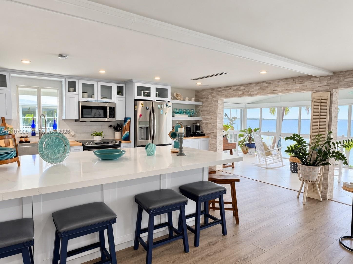 Kitchen featuring a white quartz island countertop, stainless steel appliances, white cabinetry with glass-front uppers, stacked stone accent wall, and wood-finish flooring