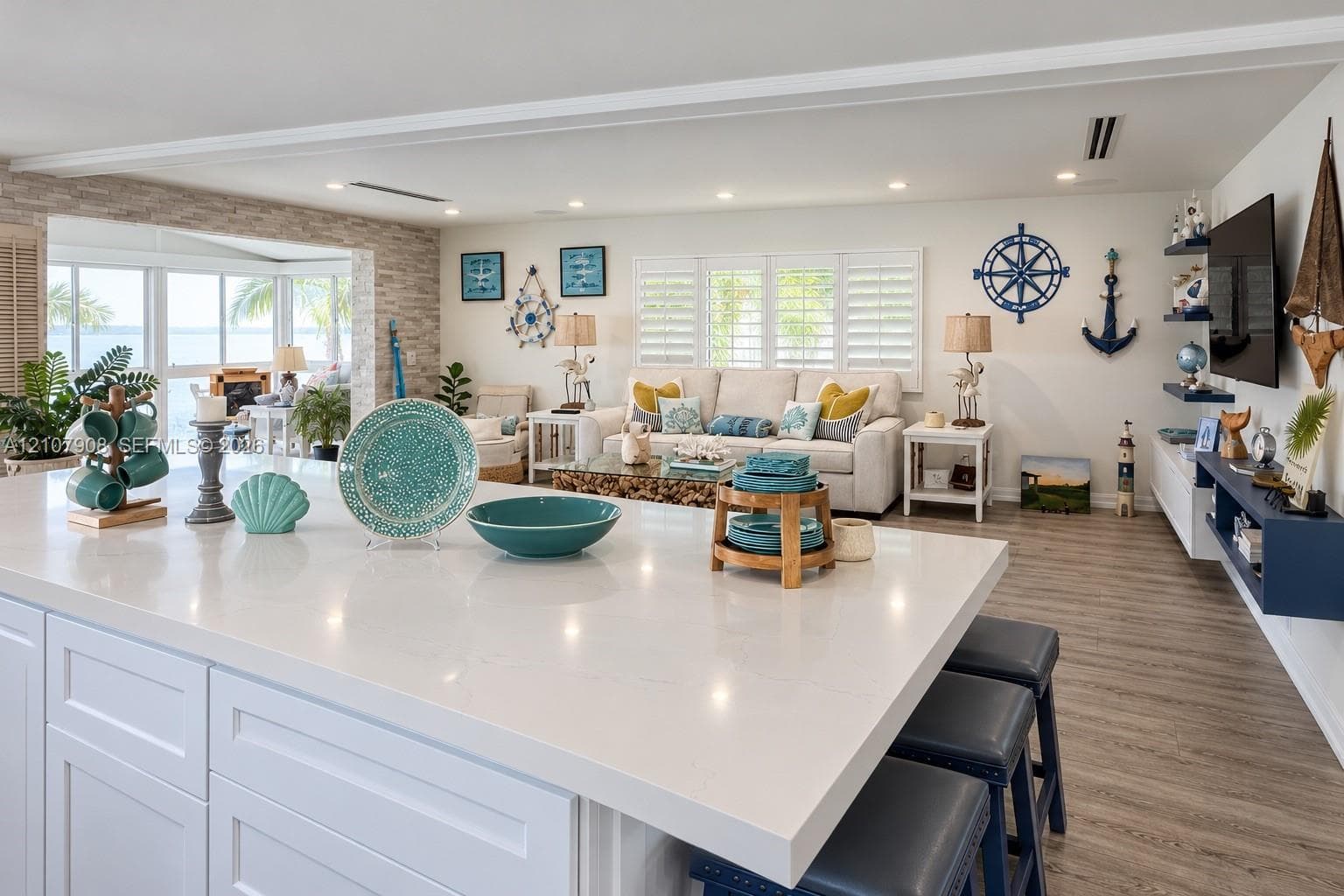 Oversized kitchen island with quartz countertop, light wood-finish flooring, stone-textured accent wall, recessed lighting, and white plantation shutters