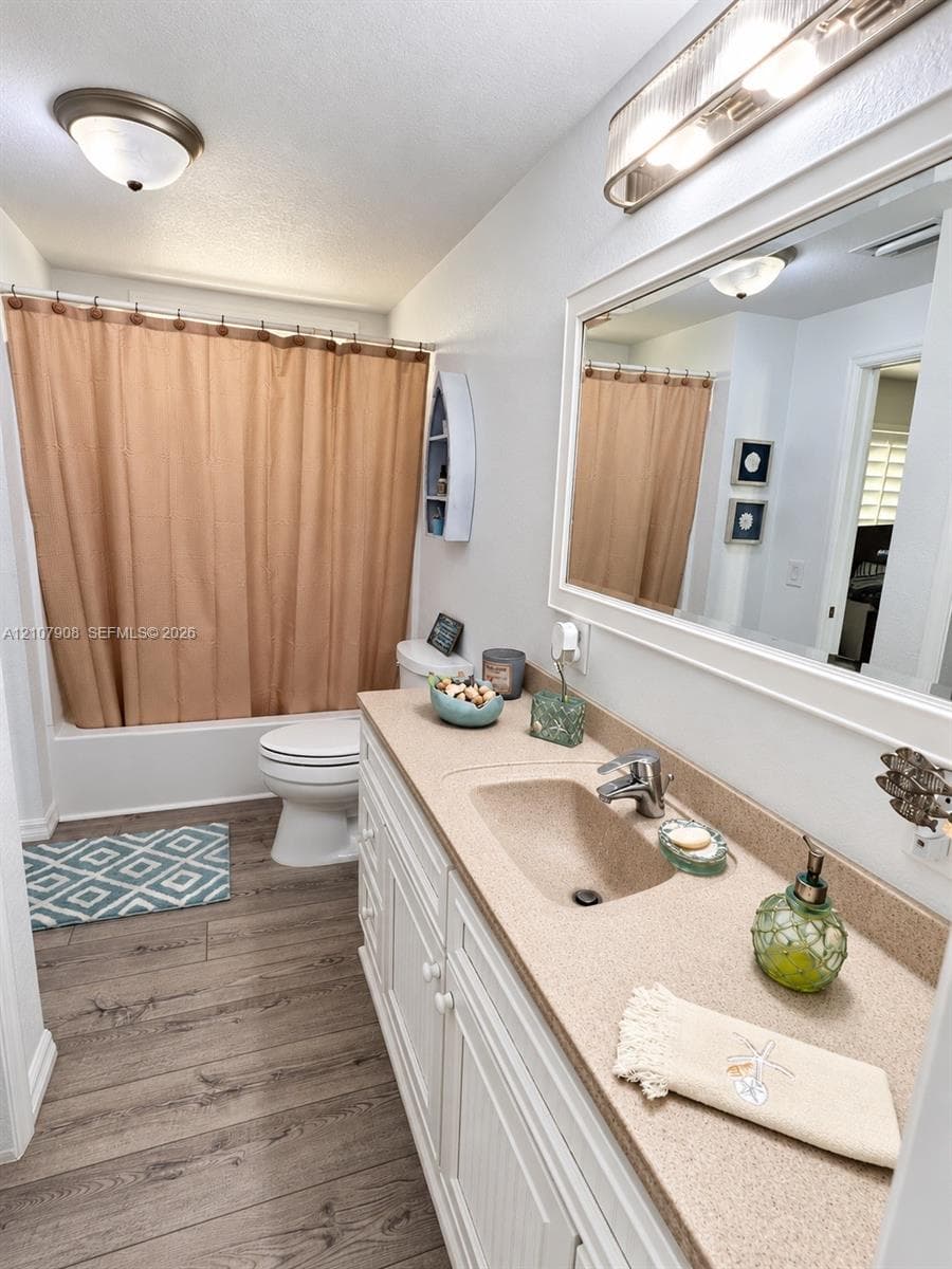 Bathroom featuring wood-finish flooring, a white vanity with an integrated sink and solid-surface countertop, a polished chrome single-lever faucet, and a wall-mounted vanity mirror with a white frame
