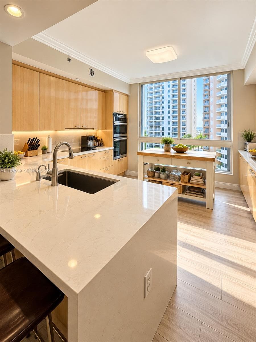 Kitchen featuring light-tone cabinetry, stone-surface countertops, built-in double wall ovens, a deep under-mount sink with a high-arch faucet, and wood-finish flooring