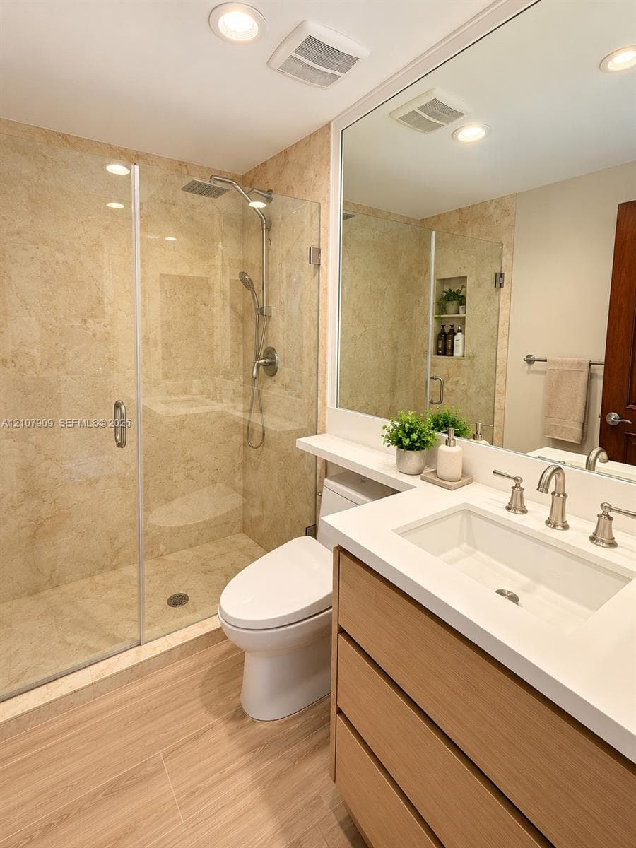 Bathroom featuring a frameless glass walk-in shower with stone wall tile, wood-finish cabinetry, quartz countertop with an integrated rectangular basin, and recessed lighting